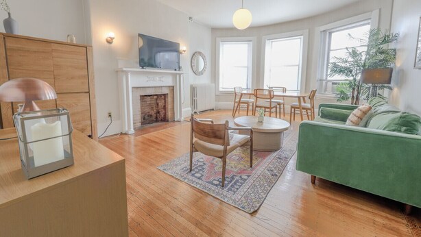 Ein Wohnzimmer mit Kamin, einem grünen Sofa, einem Esstisch mit Stühlen und einem großen Fenster.