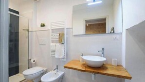 A modern bathroom with a glass shower enclosure, a toilet, a bidet, and a wooden vanity with a sink. - Urban Flat Garibaldi 36 (Bari)