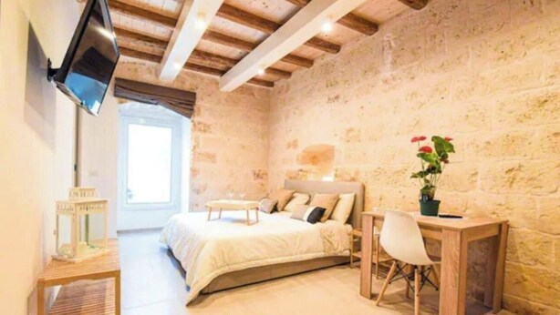 A bedroom with a stone wall, wooden ceiling beams, a bed, a desk, and a chair. - Urban Flat Garibaldi 36 (Bari)