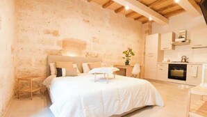 A bedroom with a large bed, a bedside table, and a nightstand. There is a kitchen area with cabinets and a stove. - Urban Flat Garibaldi 36 (Bari)