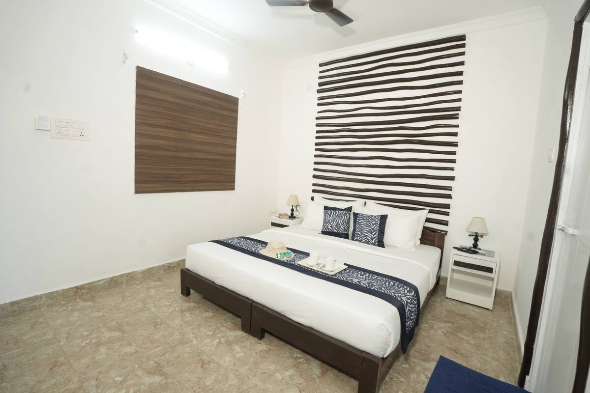 A bedroom with a bed, bedside tables, a ceiling fan, and a wall with a striped pattern.