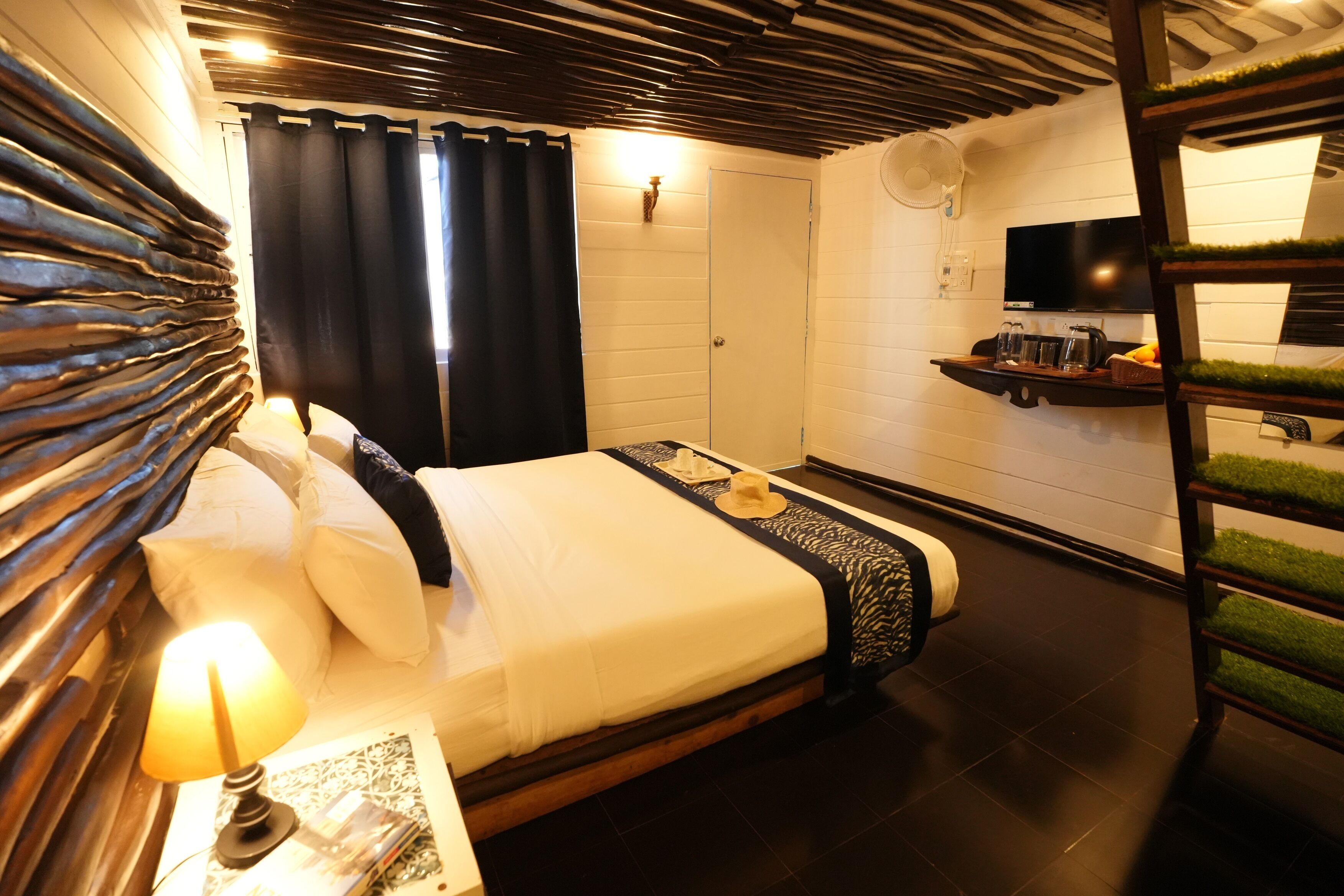 Habitación de hotel con cama, mesita de noche con lámpara, televisor en una estantería y zona de ducha.
