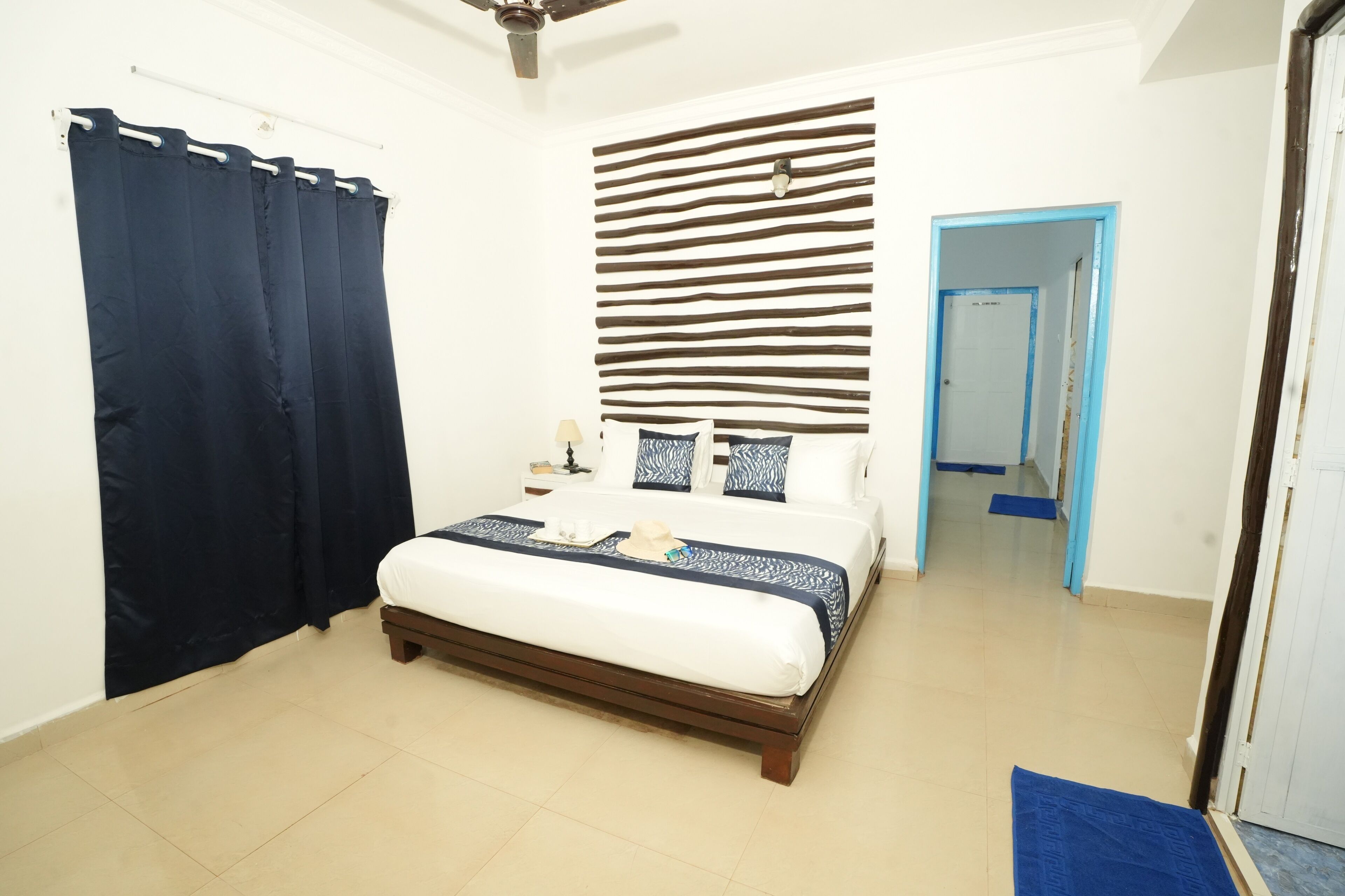 A bedroom with a bed, a ceiling fan, a dark curtain, a patterned headboard, and a blue-framed door.