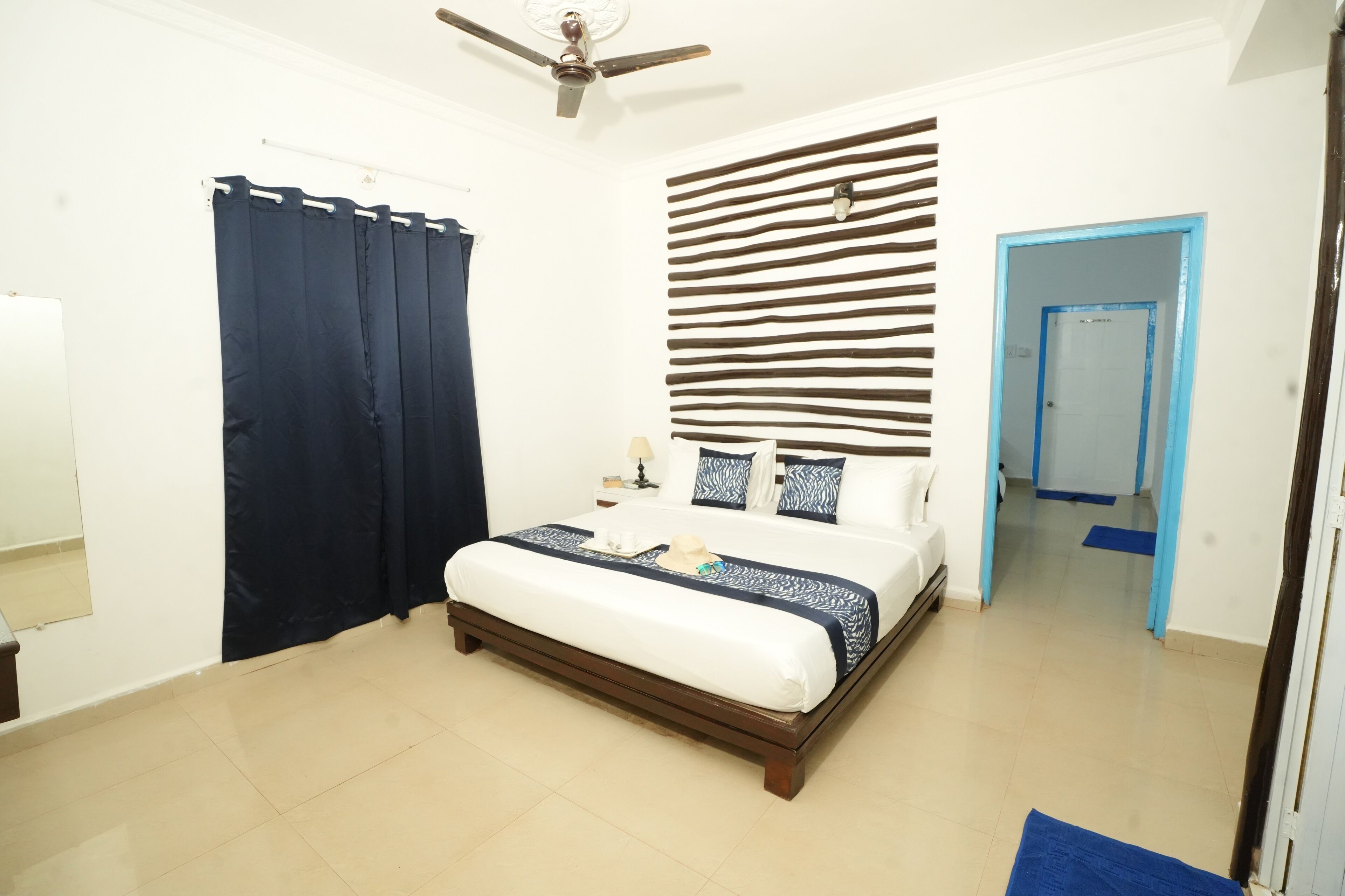 Ein Schlafzimmer mit einem Bett, einem Deckenventilator, einem Vorhang, einer Wand mit horizontalen Linien und einer Tür.