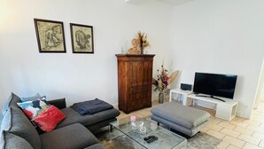 Ein modernes Wohnzimmer mit Sofa, Couchtisch und Fernseher. An der Wand hängen zwei gerahmte Bilder und ein Holzkasten steht dort.