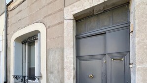 Ein Gebäude mit einer steinernen Fassade, einer grauen Doppeltür mit Messinggriff und einem Fenster mit Metallrahmen.