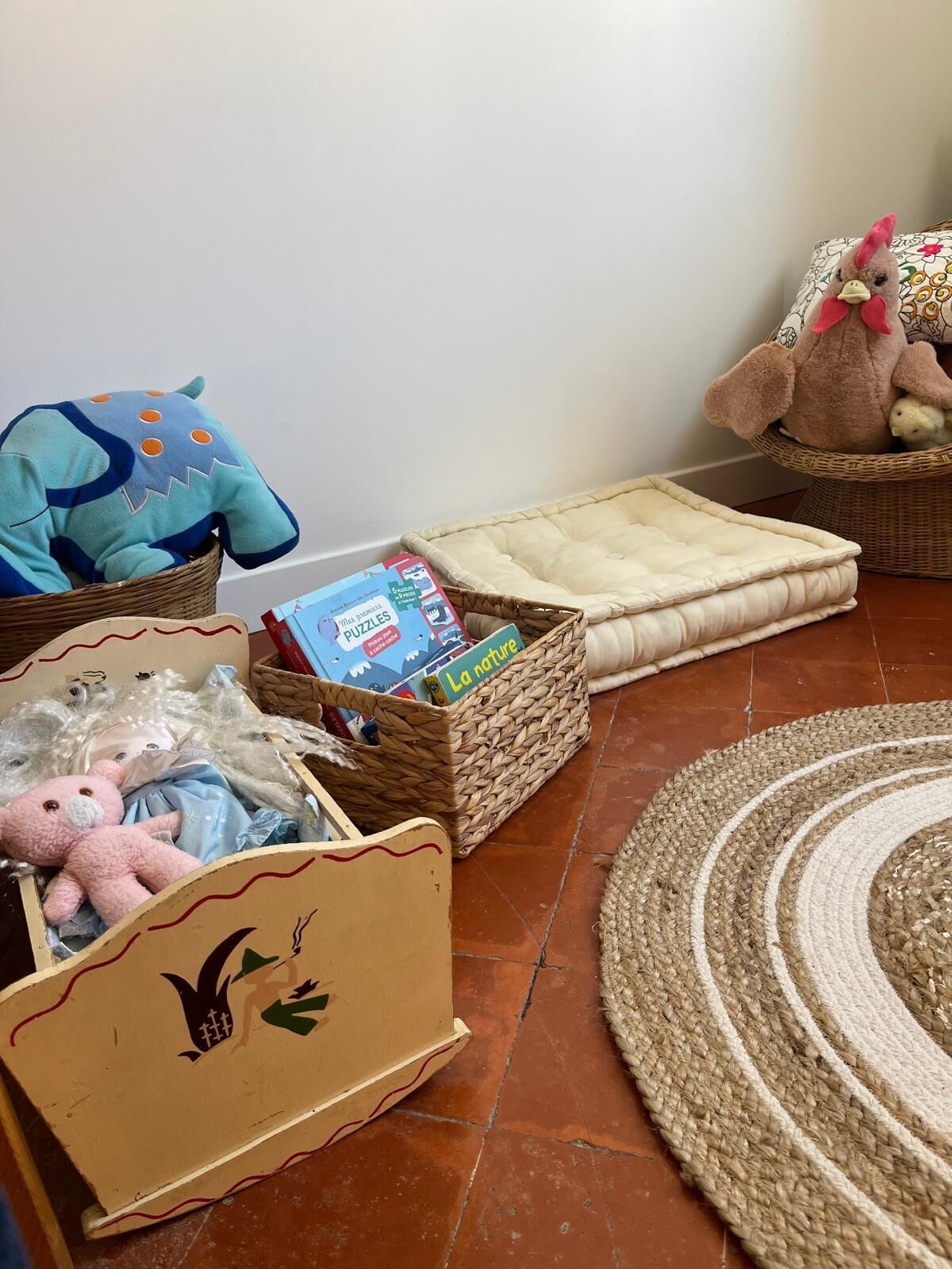 Una habitación con una cesta de mimbre que contiene un libro, un peluche y un cojín.