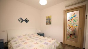 Ein Schlafzimmer mit einem blumigen Bettüberwurf, einem Nachttisch, einem Wandbild und einer Tür mit farbenfrohem Dekor.
