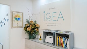 Un espace d’accueil agrémenté d’une œuvre d’art encadrée, d’un vase de fleurs, d’une bibliothèque remplie de livres et d’une enseigne indiquant « IGEA HOME ».