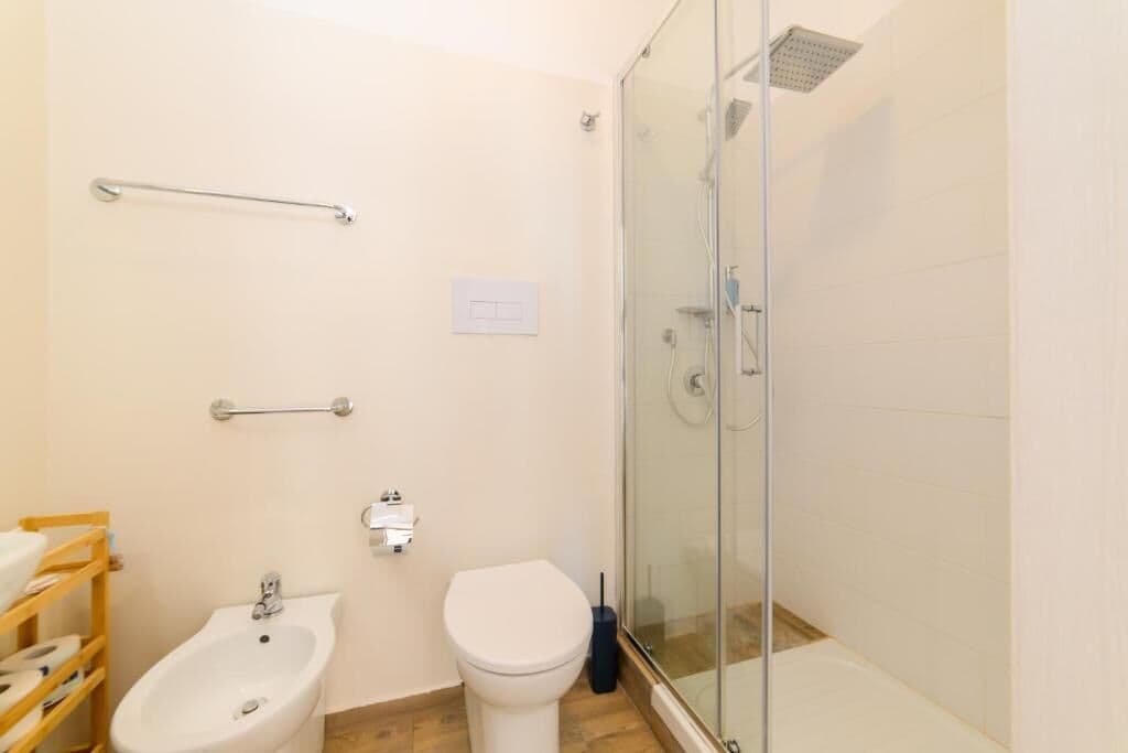 Een badkamer met een toilet, douchecabine van glas en een handgreep.