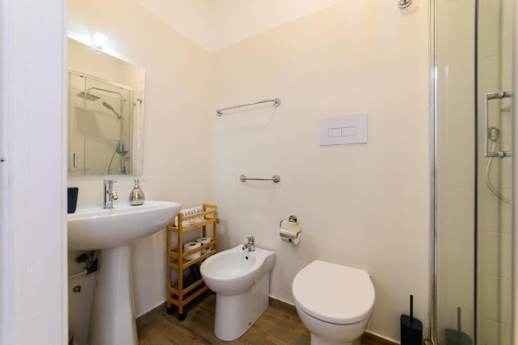 A small bathroom with a sink, bidet, toilet, and a glass shower enclosure.