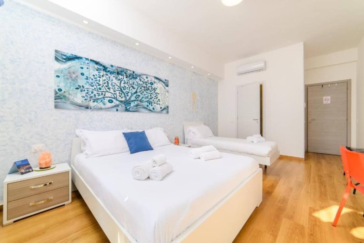 Une chambre d’hôtel avec un grand lit, deux petits lits, une table de chevet avec une lampe et un tableau au mur.