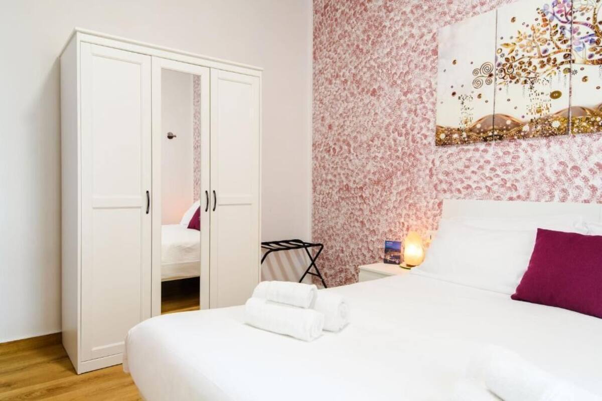 Une chambre à coucher avec un lit, une armoire blanche et un mur recouvert d’un papier peint à motifs floraux.