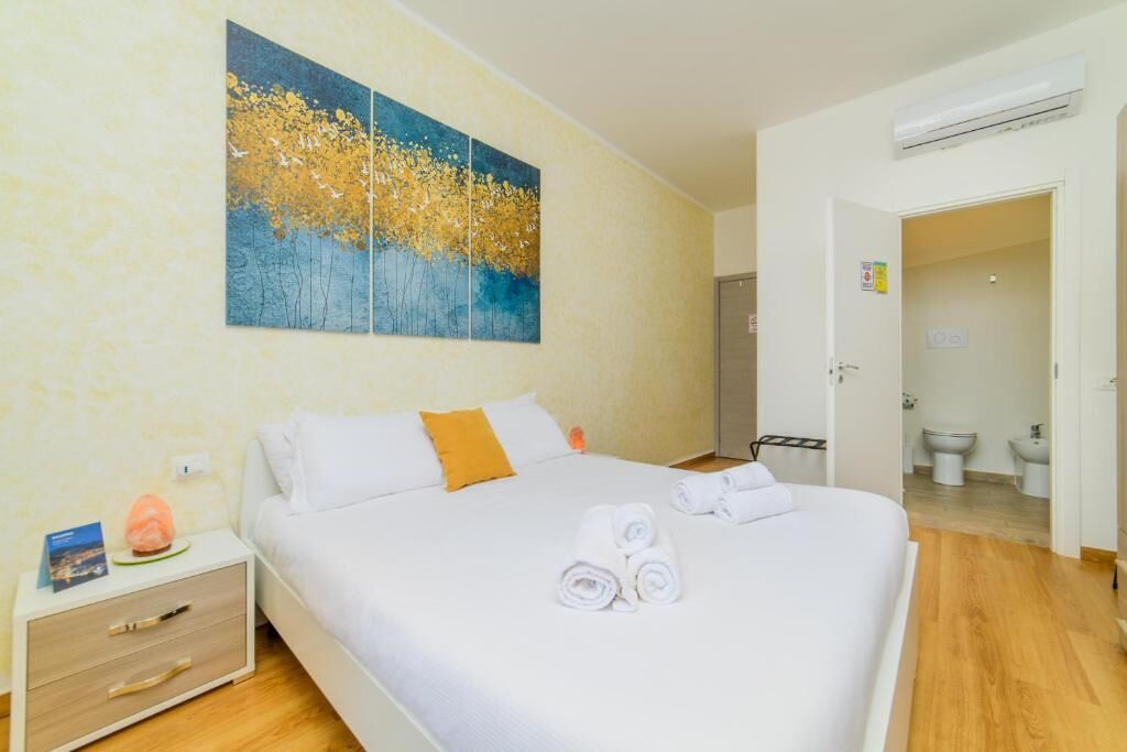 Habitación de hotel con cama, mesita de noche, un cuadro y un baño visible a través de una puerta abierta.