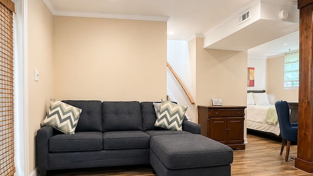 A modern living room with a sectional sofa, wooden flooring, and a staircase leading to another room.