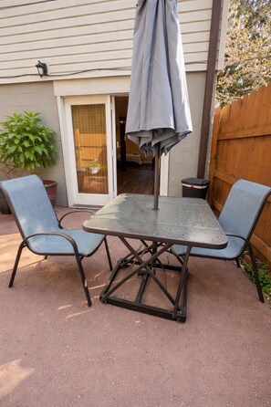 A patio with a metal table and two chairs, a grey umbrella, and a wooden fence.
