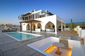 Een moderne villa met zwembad, buitenmeubilair en een woestijnlandschap op de achtergrond.