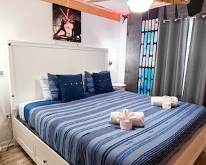 A neatly made bed with blue bedding, a wall-mounted artwork, and a curtain with a geometric pattern. - Luxury Windsor Westside Townhome | Private Pool | Across Clubhouse | Near Disney (Kissimmee)