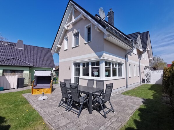 A two-story house with a bay window, a patio with a table and chairs, and a fenced yard. - Vacation home Strandburg - family-friendly, close to the beach, sauna (Zingst)