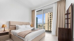 A modern hotel room with a large bed, a nightstand, a wooden wardrobe, and a balcony with a city view. - Stayshort - Elegant 1 Bedroom in Emaar Beachfront That Sleeps 2 (Dubai)