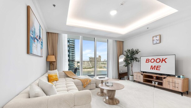 A modern living room with a sofa, a coffee table, a TV, and a view of the city. - Stayshort - Elegant 1 Bedroom in Emaar Beachfront That Sleeps 2 (Dubai)