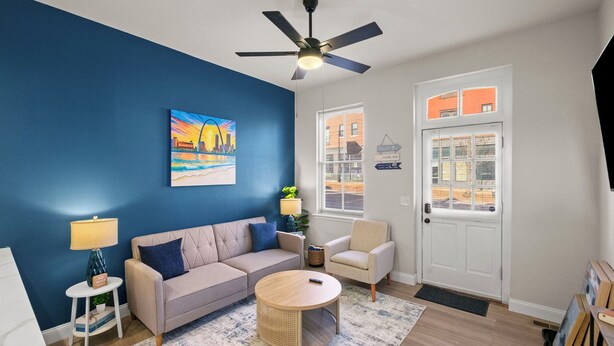 A living room with a blue wall, a ceiling fan, a sofa, a coffee table, a lamp, and a door with a window. - Cozy Beach Apartment in Soulard (St. Louis)