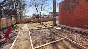 A backyard with a wooden deck, a red chair, and a brick wall. - Cozy Beach Apartment in Soulard (St. Louis)