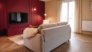 Una sala de estar moderna con televisor de pantalla plana, un sofá, una lámpara y un ventanal con cortinas.