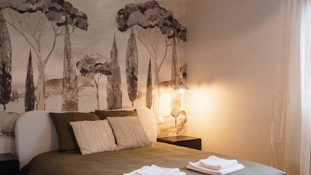 Un dormitorio con cama, mesita de noche, lámpara y un mural en la pared.