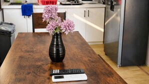 A wooden dining table with a vase of flowers, a remote control, and a smartphone.
