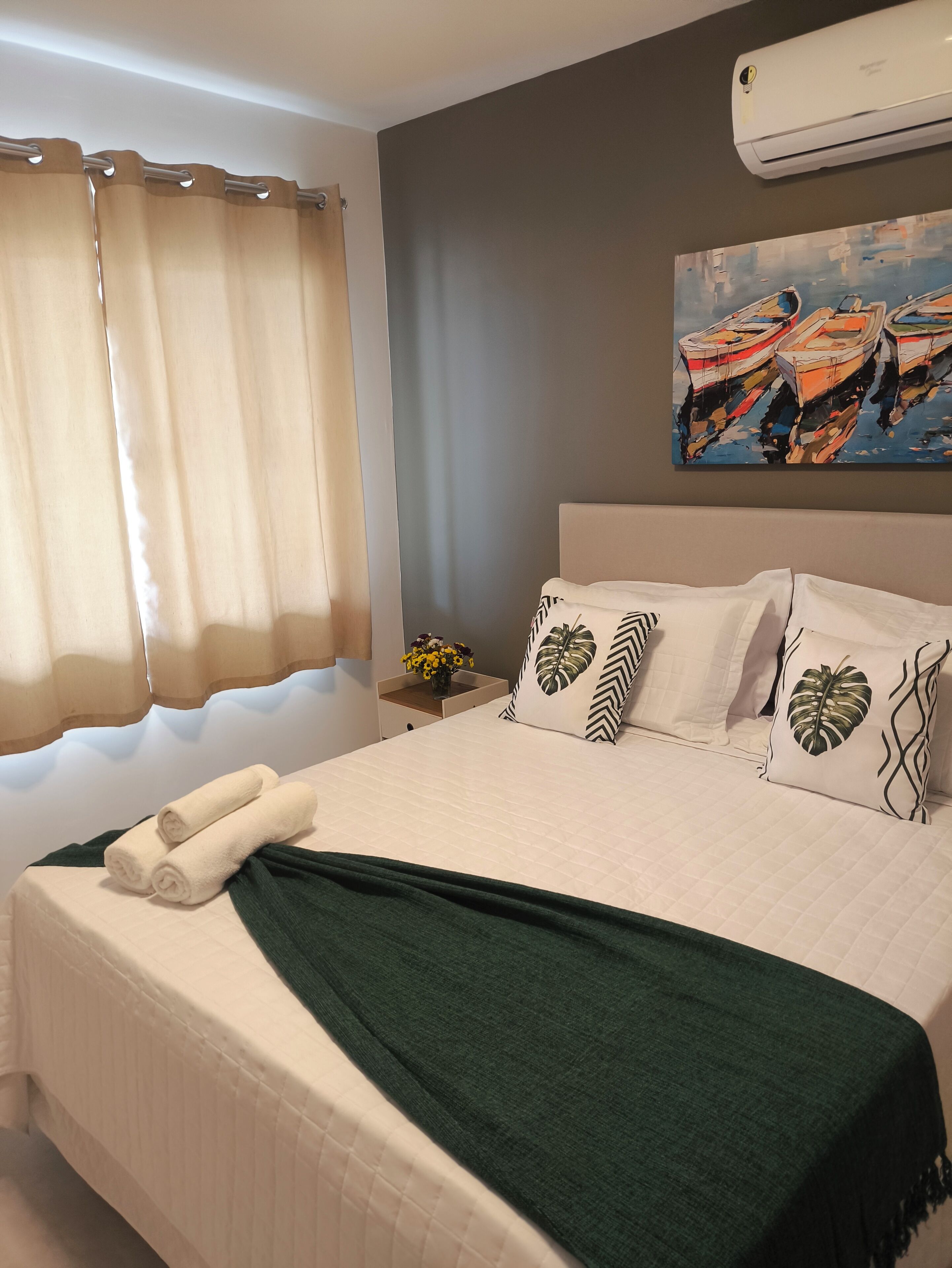 A neatly made bed with a green throw blanket, white bedding, and decorative pillows with leaf patterns.