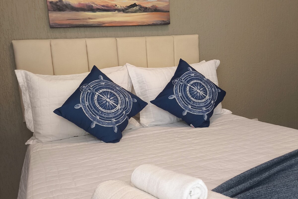A neatly made bed with white and navy blue pillows, a rolled white towel, and a blue blanket.