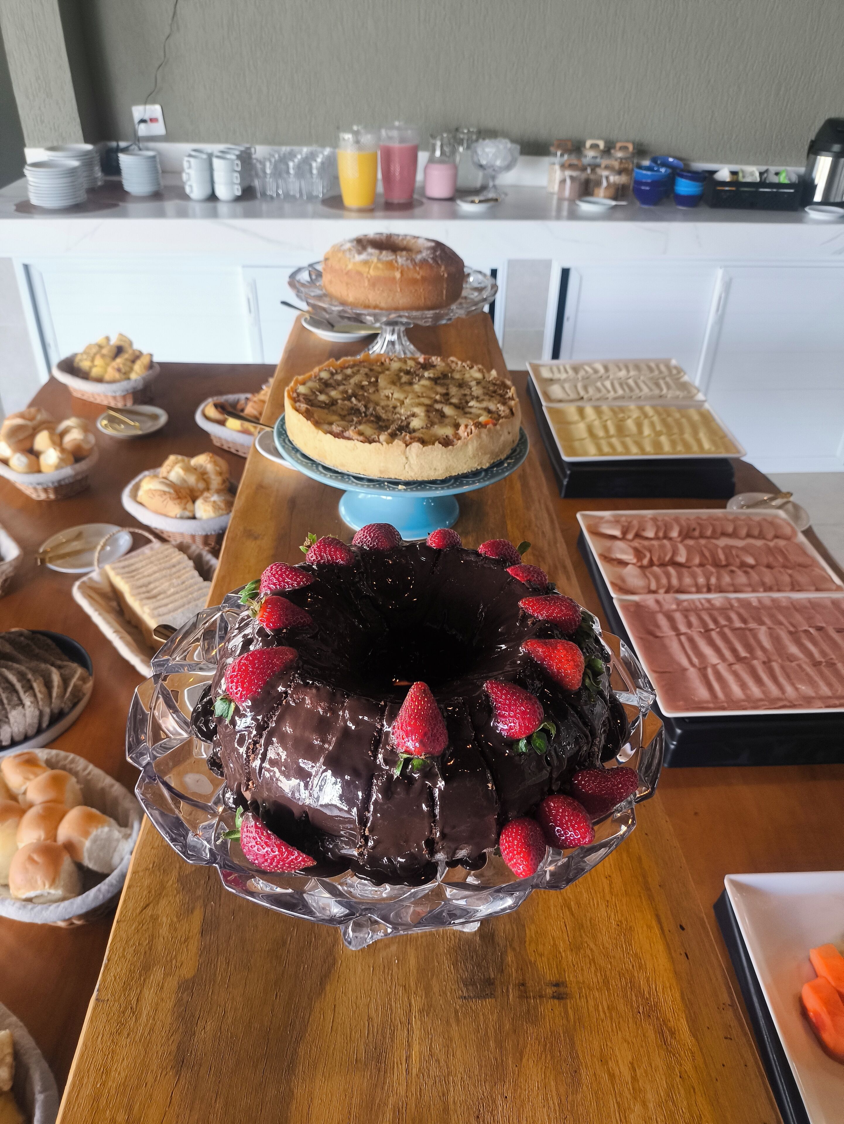 A buffet table with various desserts, including a chocolate cake with strawberries, a fruit tart, and other baked goods.
