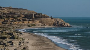 Eine Küstenlandschaft mit Steinhäusern, einem Sandstrand und dem Meer.