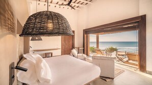 Ein Schlafzimmer mit einem Bett, einer Pendelleuchte, einem Holzschrank und Meerblick durch eine offene Tür.