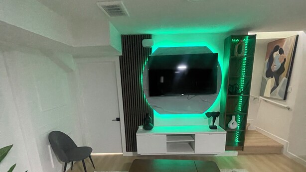 Un salon moderne avec un téléviseur à écran plat fixé sur un meuble blanc, un canapé gris, un fauteuil noir et un tapis à motifs.