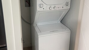 Une petite machine à laver blanche, dotée d’un panneau de commande, installée dans une petite buanderie.