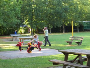 En park med picknickbord, en lekplats och en tennisbana.