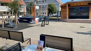 Área externa com parquinho, estrutura de madeira e um edifício com telhado inclinado.