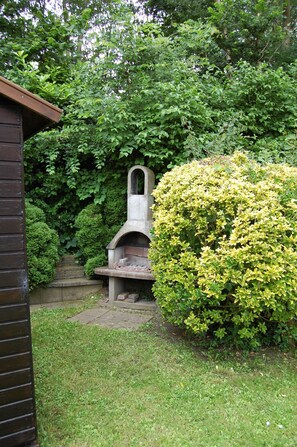 A stone-built outdoor grill in a lush garden with dense foliage and a brick wall. - Tastefully decorated family vacation home, right on the waterfront (Bruinisse)