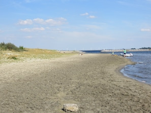 A sandy beach with a calm sea, a few people, and wind turbines in the distance. - Tastefully decorated family vacation home, right on the waterfront (Bruinisse)