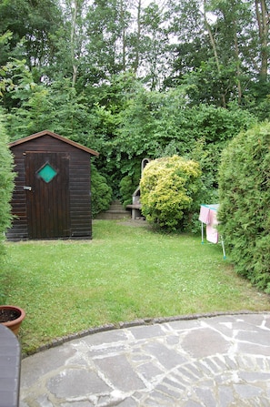 A wooden shed with a green window, surrounded by lush greenery and a stone pathway. - Tastefully decorated family vacation home, right on the waterfront (Bruinisse)