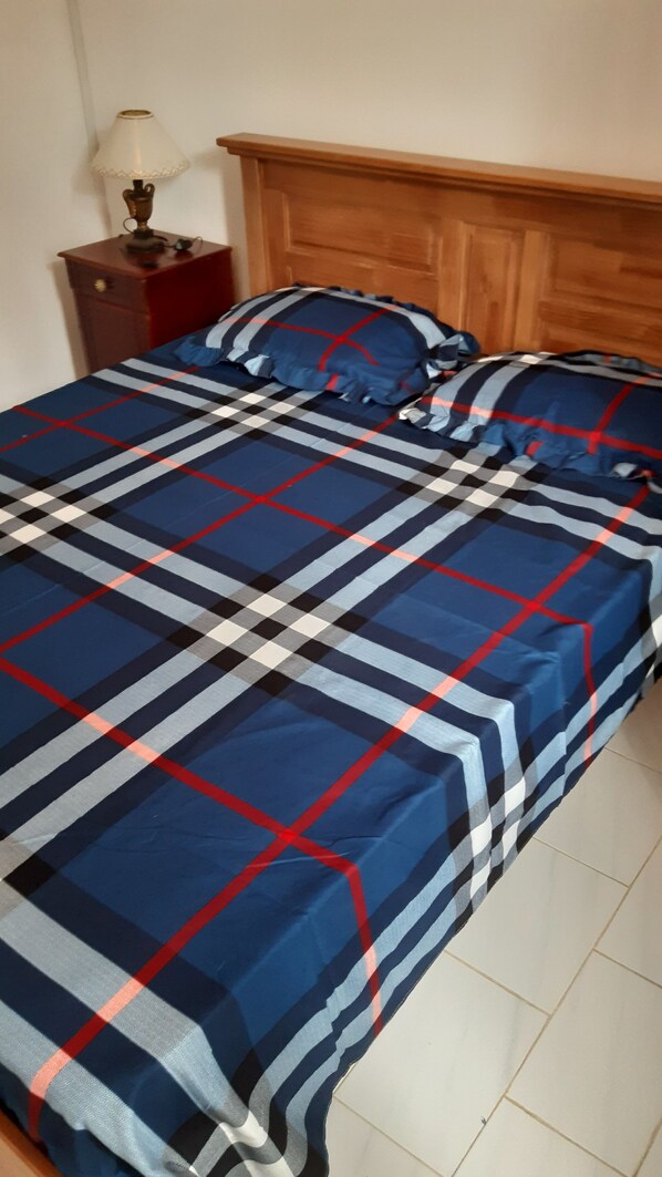 A bed with a plaid bedspread, a wooden headboard, and a nightstand with a lamp.