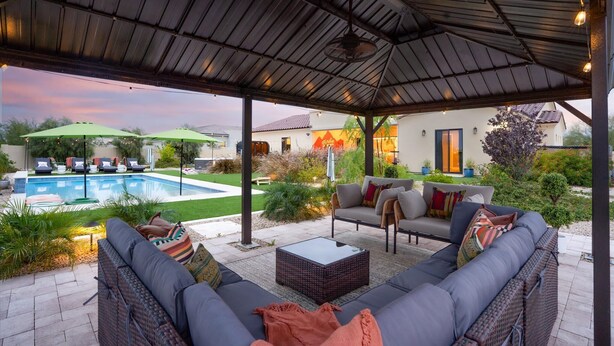Un'area patio esterna con una zona salotto coperta, una piscina e una casa sullo sfondo.