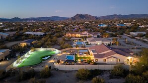 Un quartiere residenziale con una grande casa dotata di piscina, campo da tennis e un giardino curato.