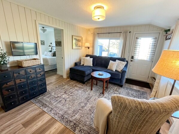 A cozy living room with a dark blue sofa, a round coffee table, and a patterned rug. There is a television on a stand, a dresser with drawers, and a lamp on a side table. - Family-ready cabin with dedicated boat slip at walkable marina and beach access. (International Falls)
