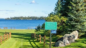 Un panneau indiquant l’accès à la plage publique de Point of Pines, avec des tables de pique-nique et une vue sur l’eau.