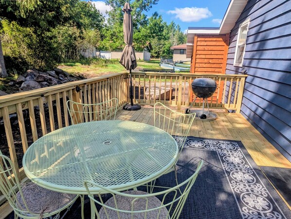 Een terras met een ronde tafel en stoelen, een barbecue en een parasol.