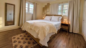 Quarto com cama, ventilador de teto, mesa de cabeceira, luminária, janela e porta.