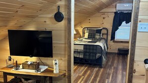 A cozy wooden cabin room with a bed, a TV, and a small table with candles. - Charming Cabin - Wake up to the Epic Views, Stay for the Convenience (Carlisle)